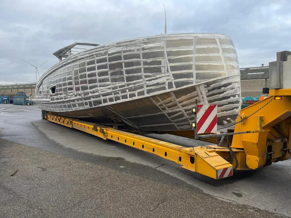 Bare aluminum hull on a yellow trailer with wind turbines.
