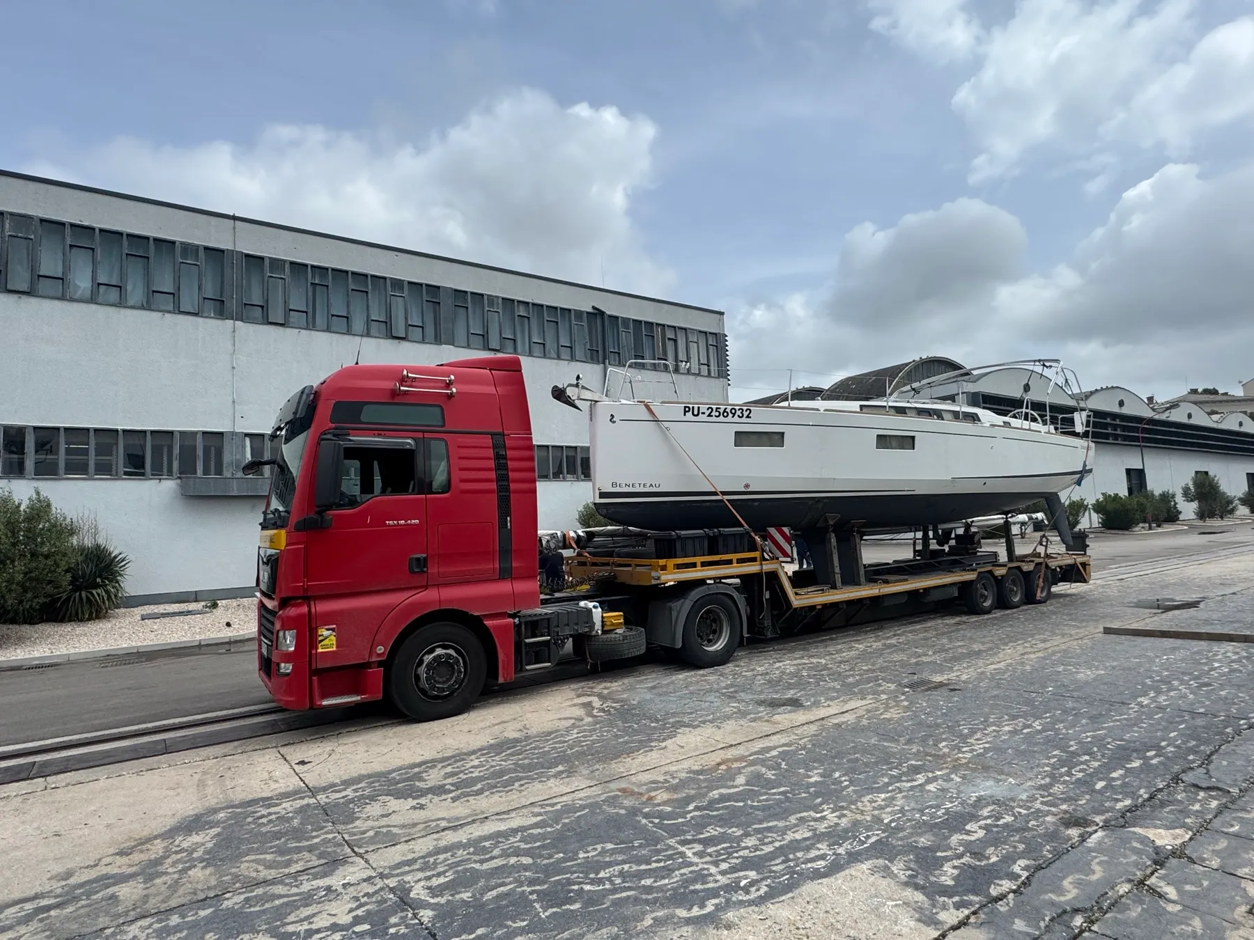 White Beneteau sailing yacht on a low-loader at a boatyard.
