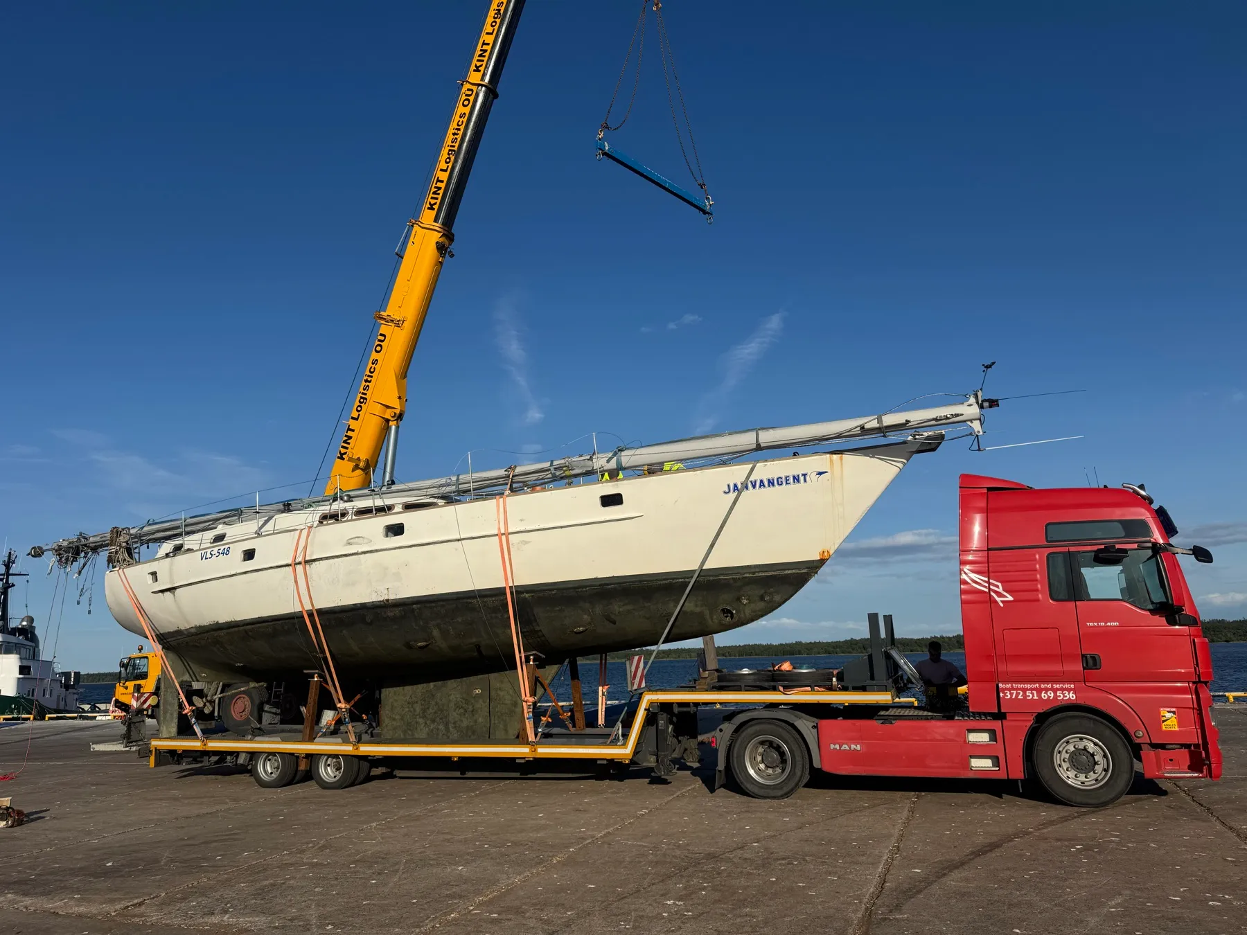 Sailing yacht being craned onto a red truck low-loader.