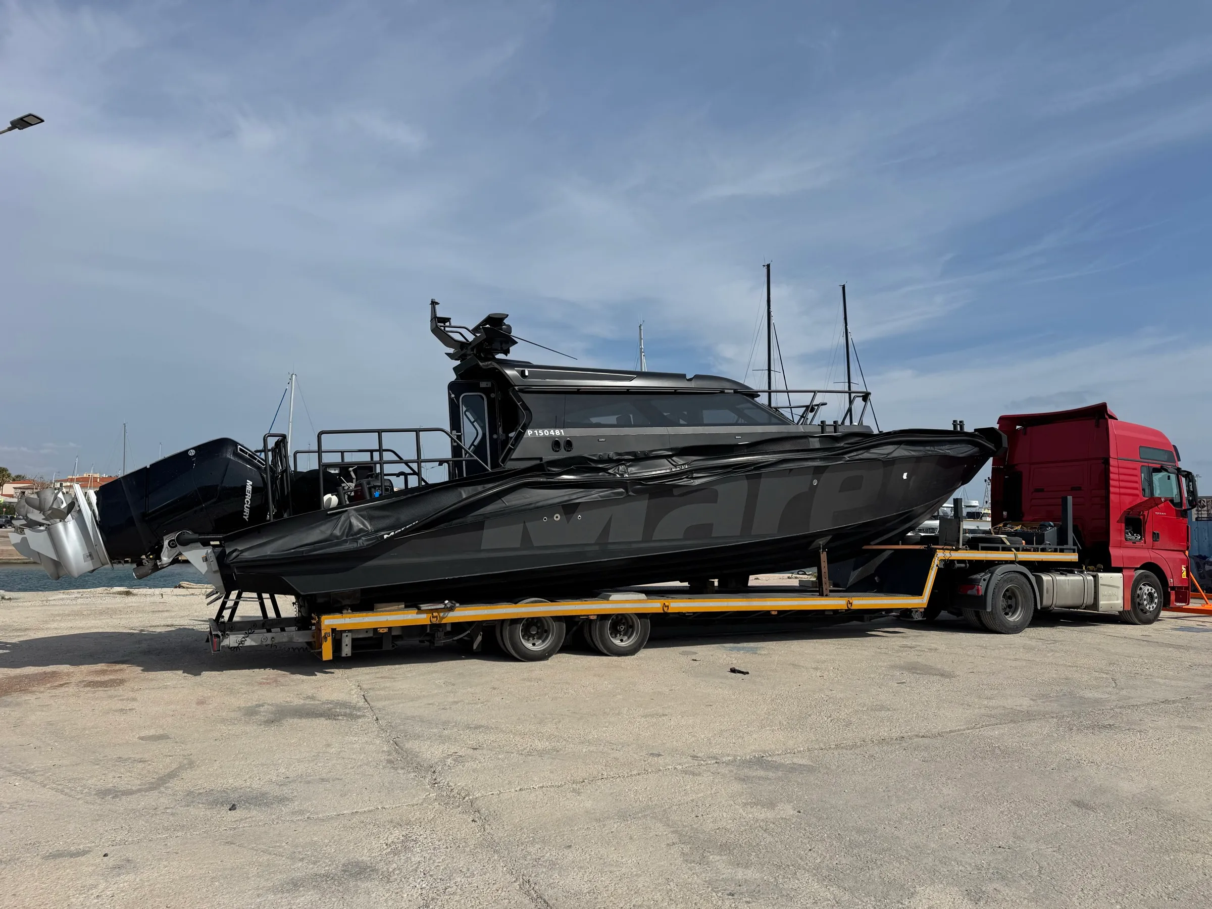 Sleek black Marex powerboat on a yellow low-loader at a marina.