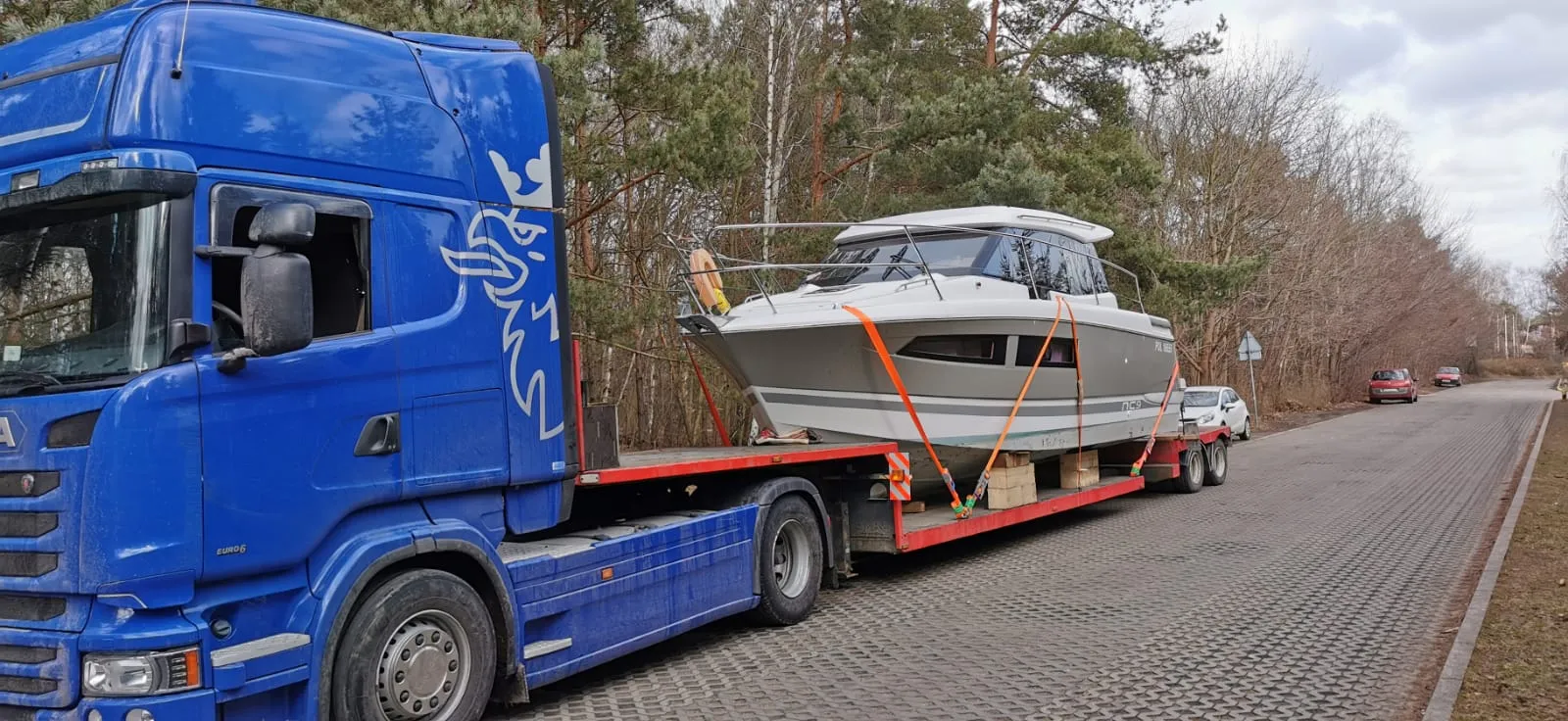 Blue Scania tractor with white motorboat on a low-loader.