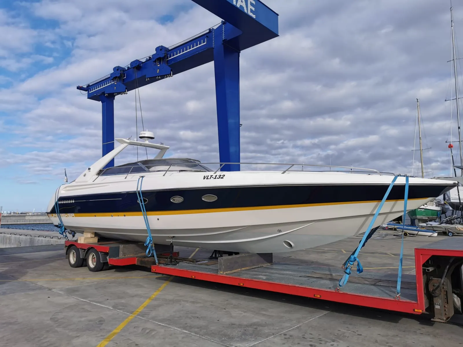 Sunseeker cabin cruiser being lifted onto a trailer under a marina gantry crane.
