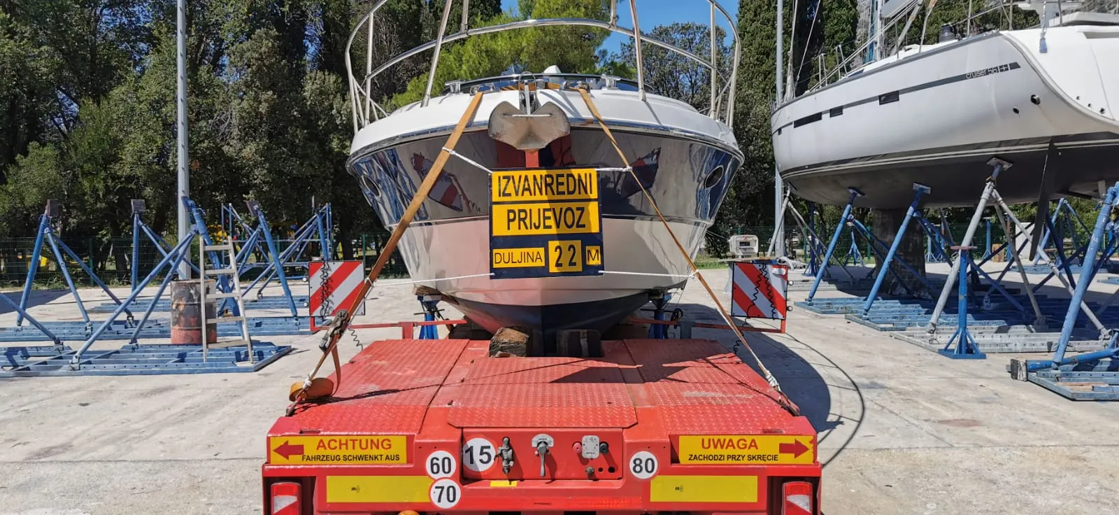Yacht on a low-loader trailer with Croatian oversize-load placards.