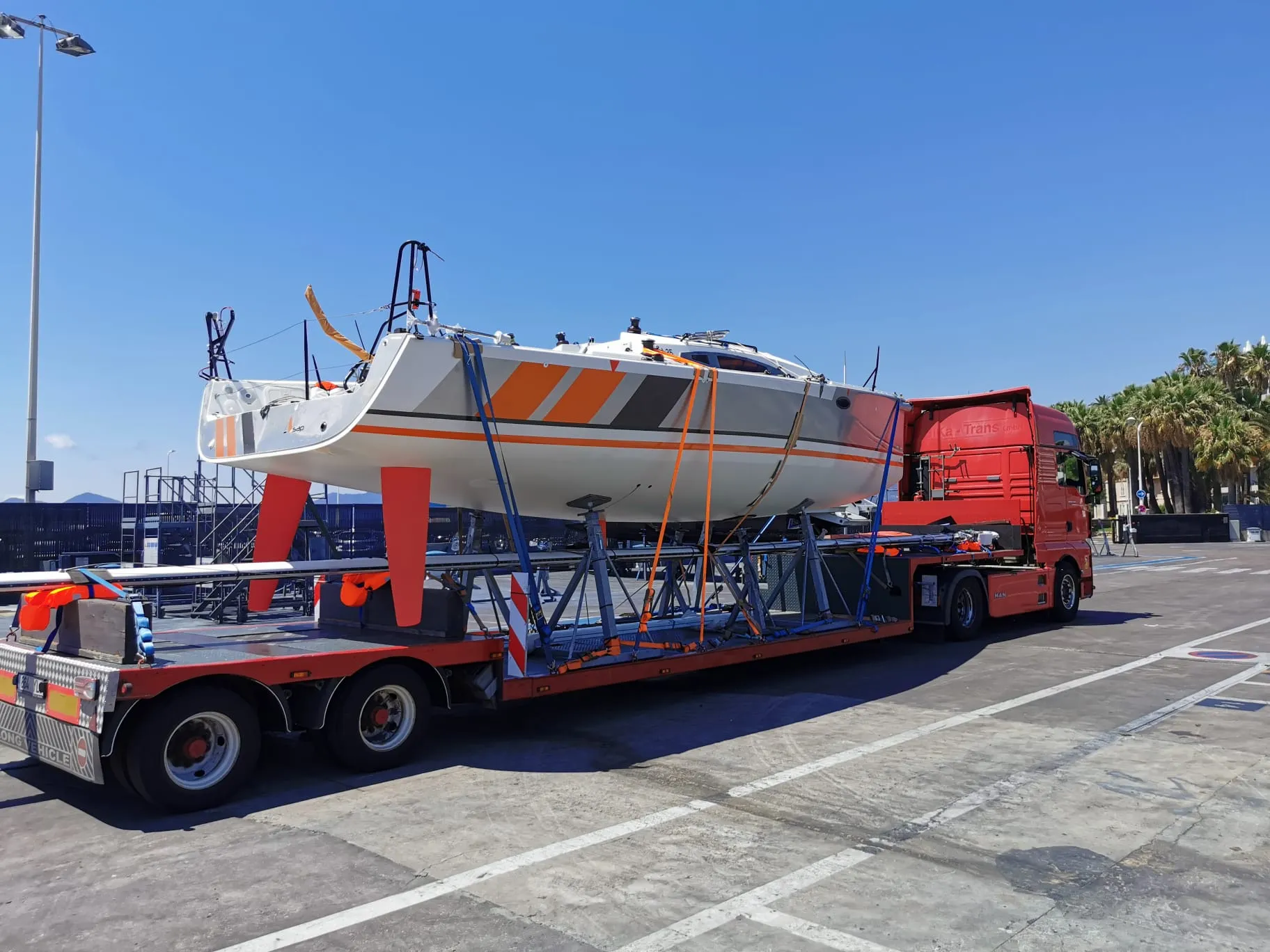 Racing yacht with orange graphics secured on a low-loader trailer.